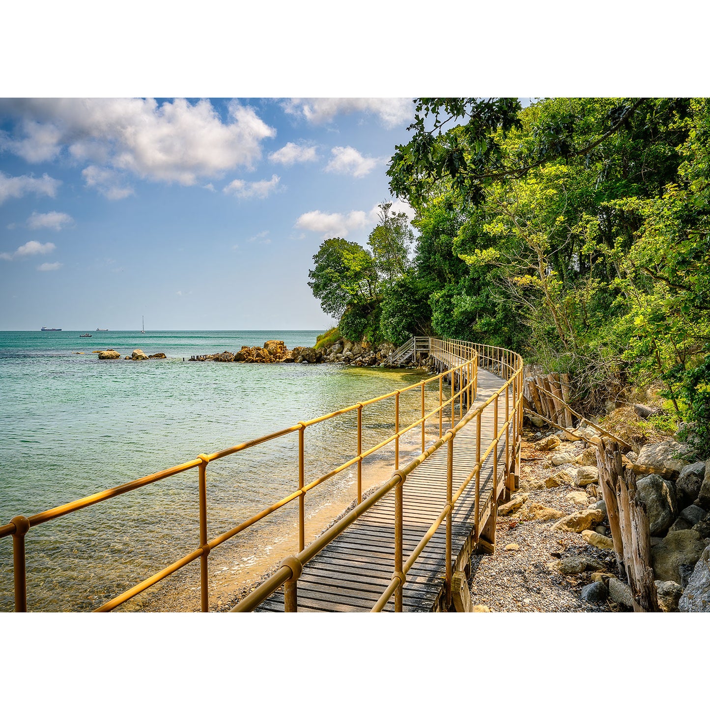 Seagrove Bay boardwalk along a rocky shoreline with lush greenery under a clear sky on the Isle of Wight by Available Light Photography.