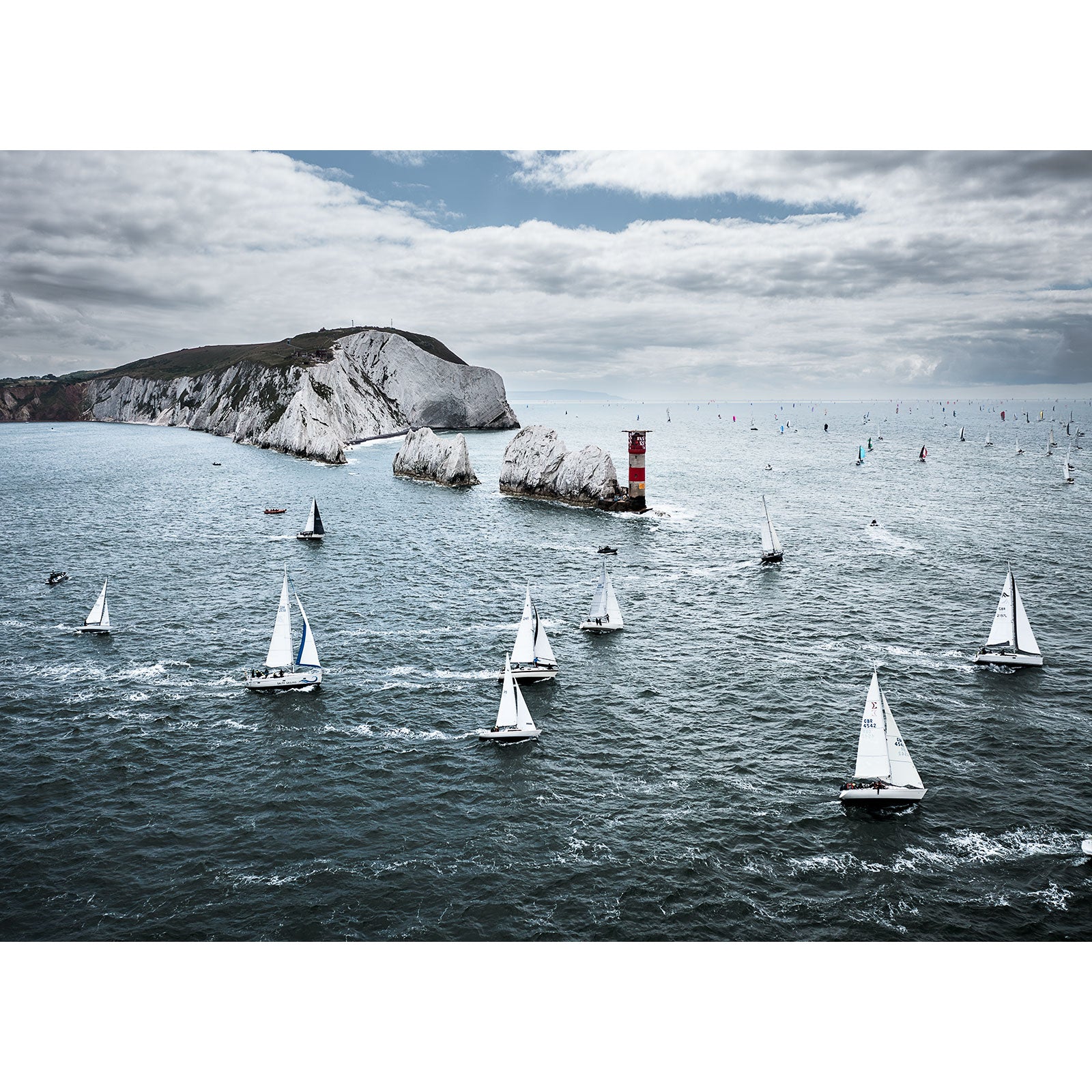 Sailboats racing near a coastal headland with a red lighthouse beacon on the Isle of Wight in the Round the Island Race 2023 captured by Available Light Photography.