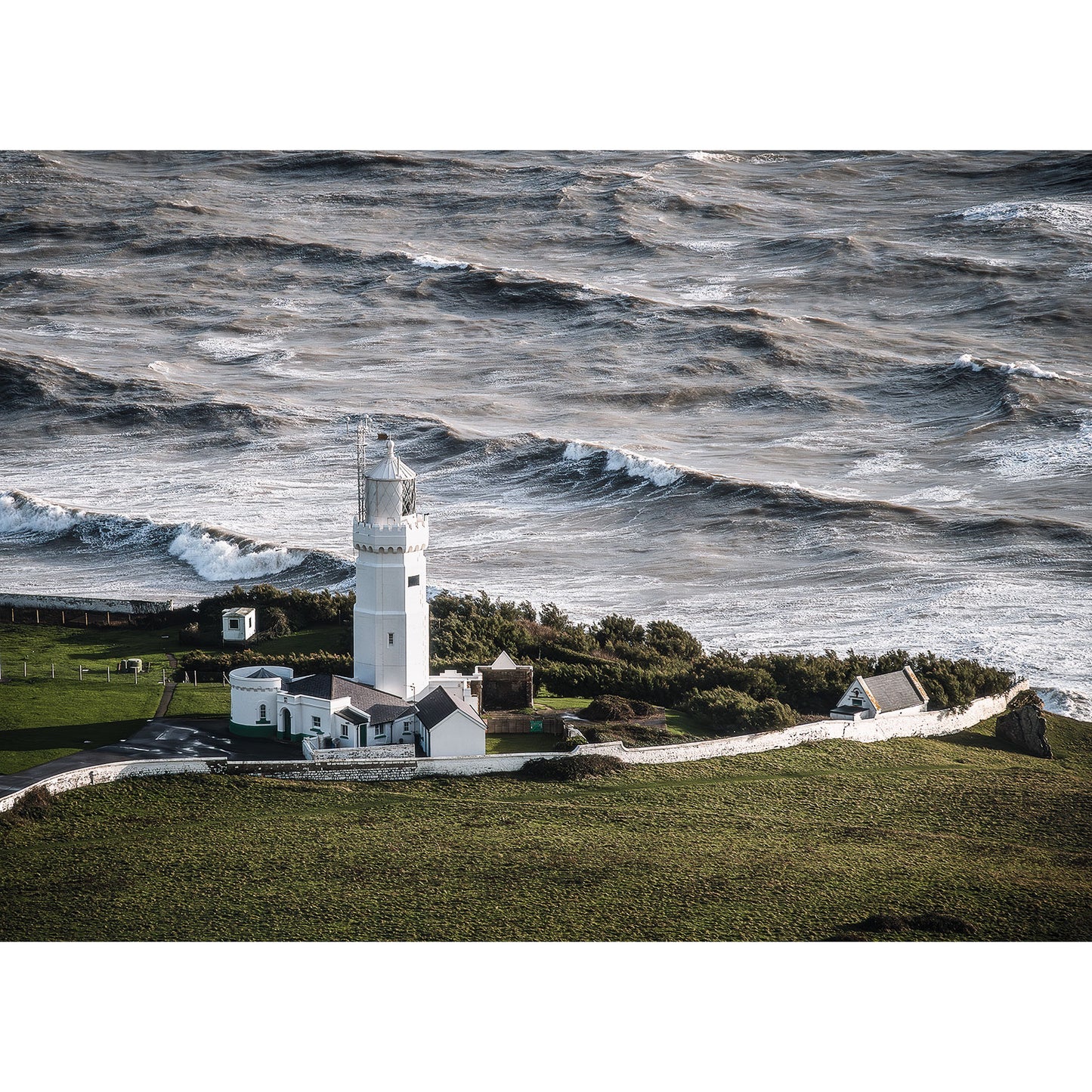 A Stormy Seas lighthouse stands on the Isle of Wight's coastal headland above turbulent sea waves, captured by Available Light Photography.