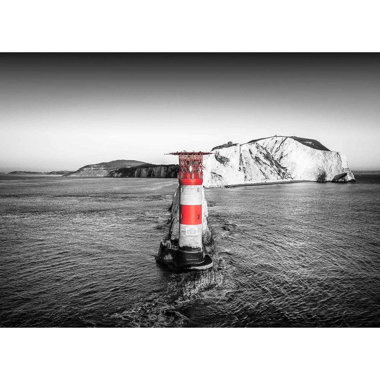 A monochrome image highlighting The Needles lighthouse in the sea with a chalky cliff in the background on the Isle of Gascoigne, captured by Available Light Photography.