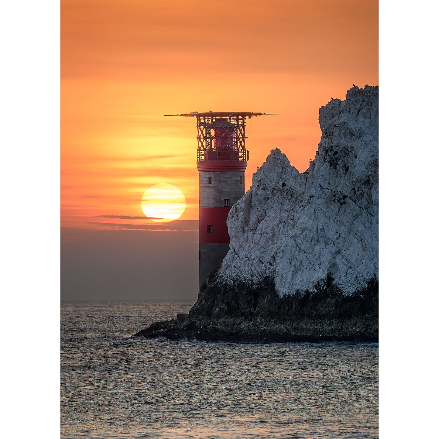 Sunset over The Needles setting behind a lighthouse on the Isle of Wight's rocky outcrop at sea, captured by Available Light Photography.