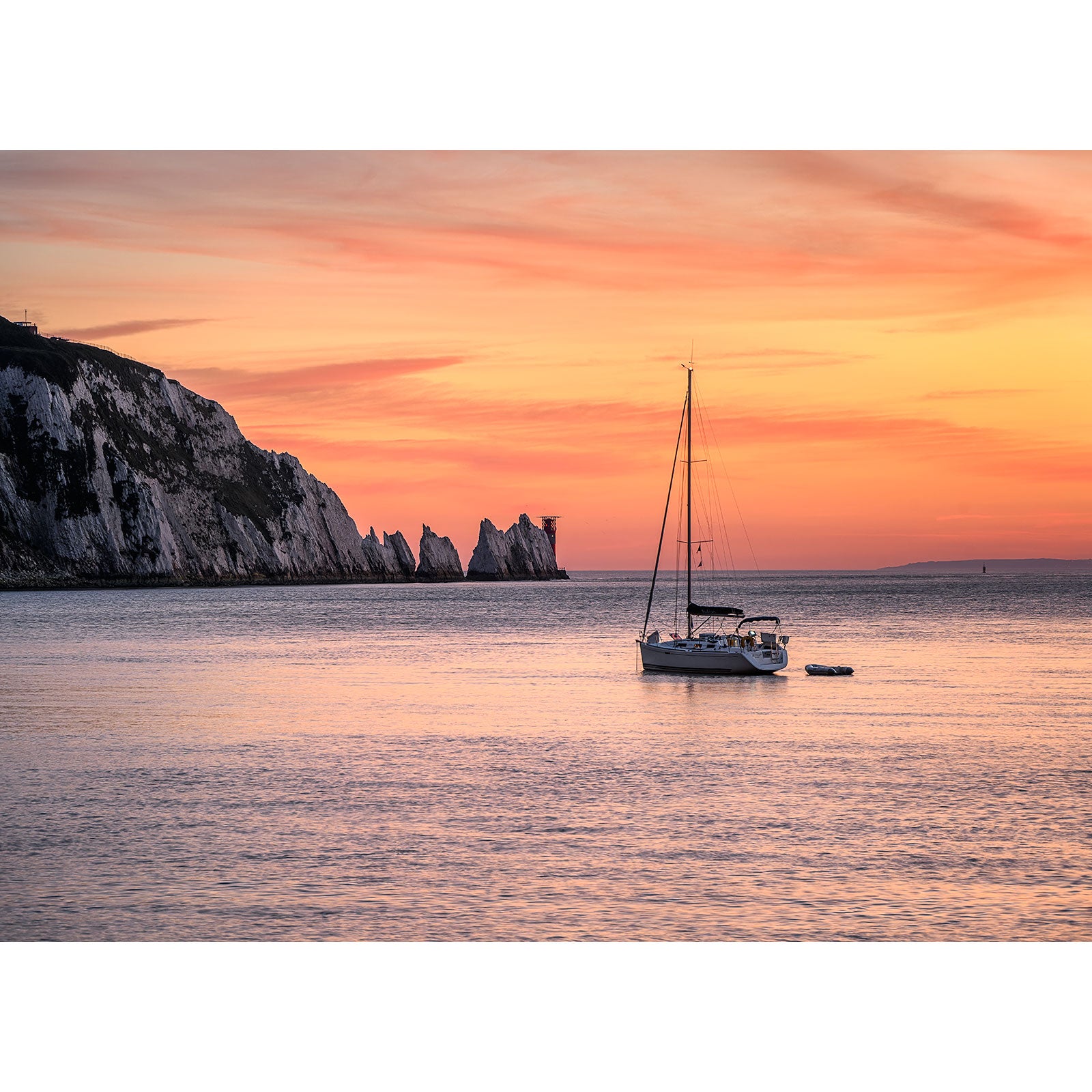 Sailboat anchored near a cliff at sunset on the Isle of Wight featuring The Needles by Available Light Photography.