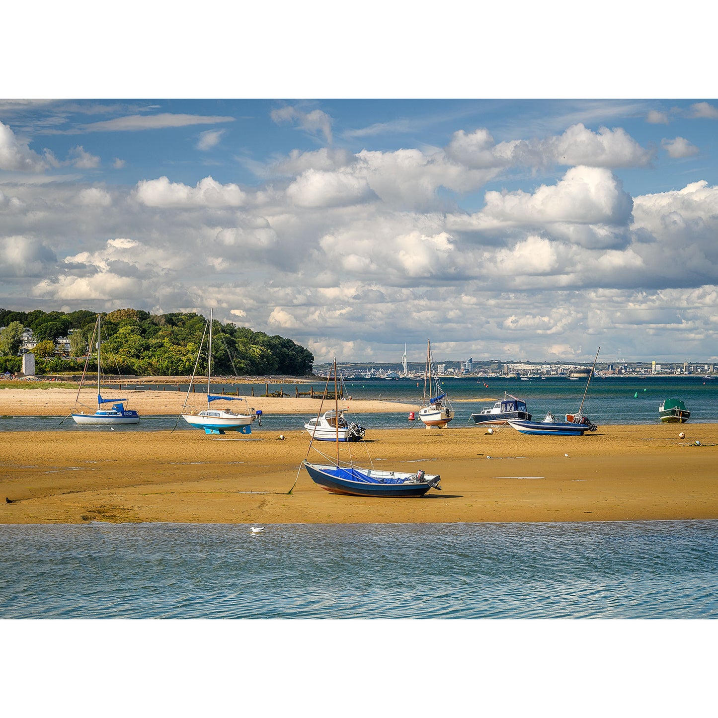 A serene low-tide scene at Bembridge Harbour on the Isle of Wight with boats on a sandy shore under a partly cloudy sky, captured by Available Light Photography.