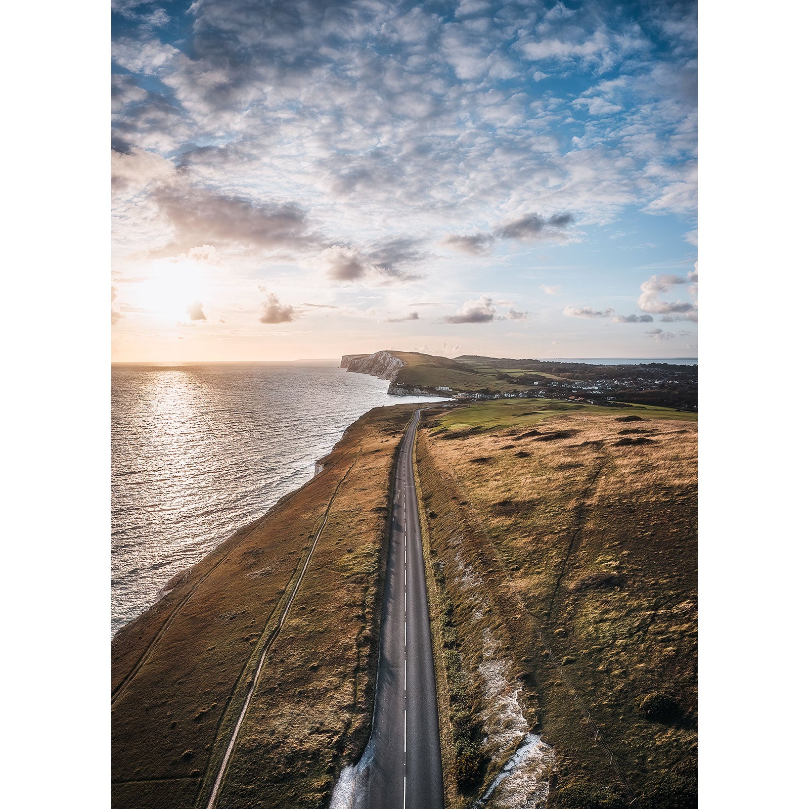 Coastal road leading towards cliffs under a cloudy sky at sunset on the Isle of Wight, featuring The Military Road by Available Light Photography.