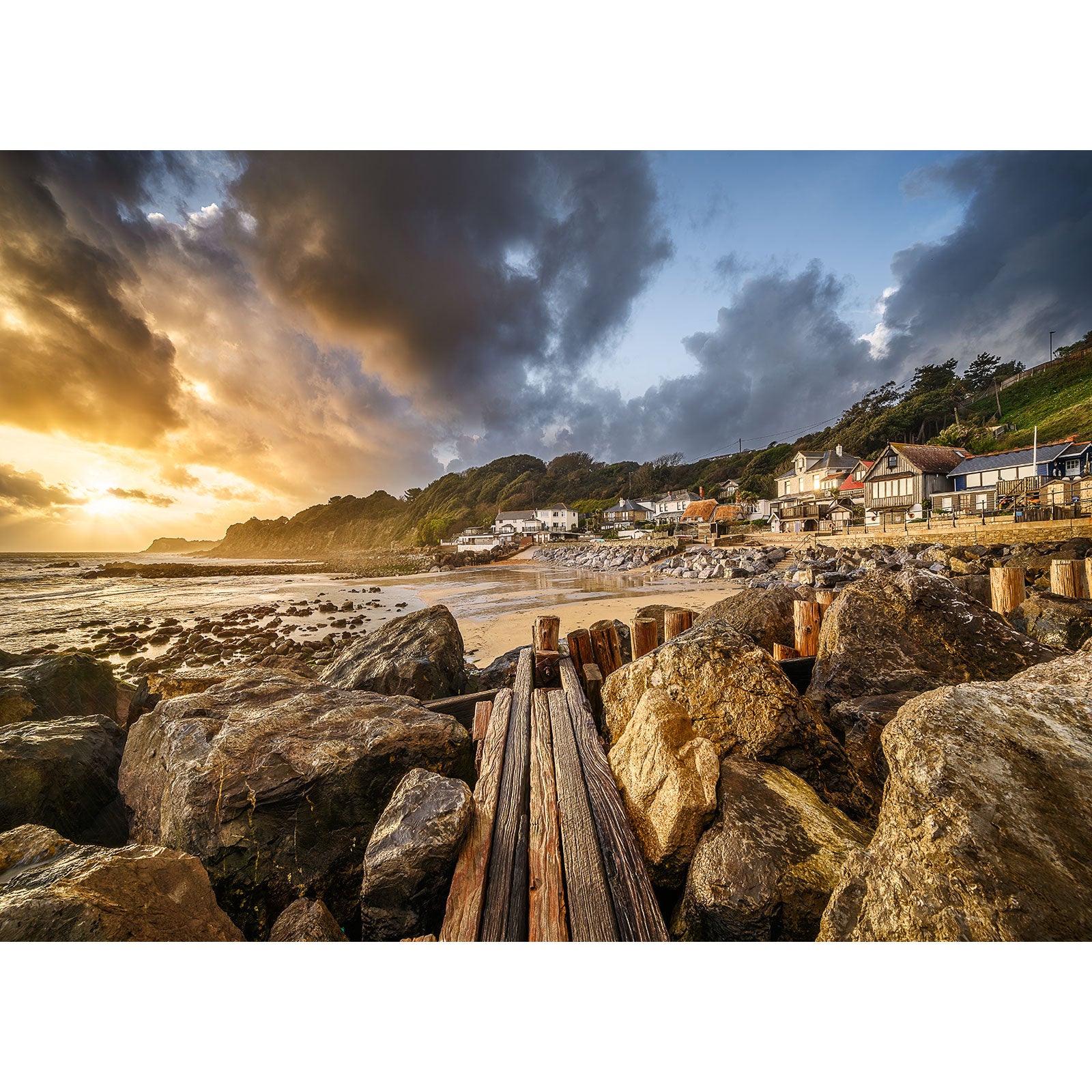 A scenic coastal village at sunset with a rustic wooden jetty and rocky shoreline on the Isle of Wight under a dramatic sky by Available Light Photography featuring Steephill Cove.
