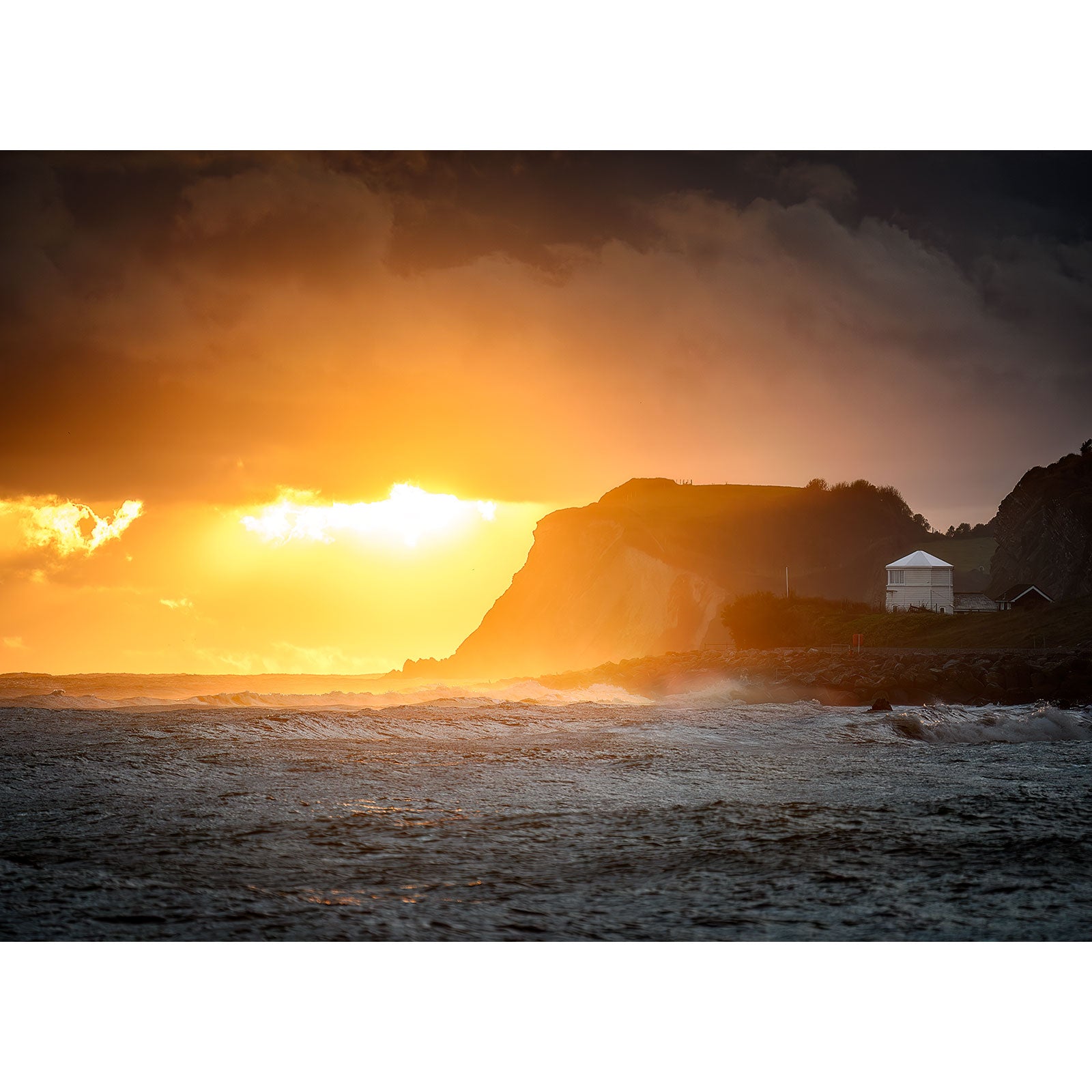 Sunset glowing behind stormy seas with silhouette of cliffs in the background on the Isle of Wight captured by Woody Point from Ventnor by Available Light Photography.