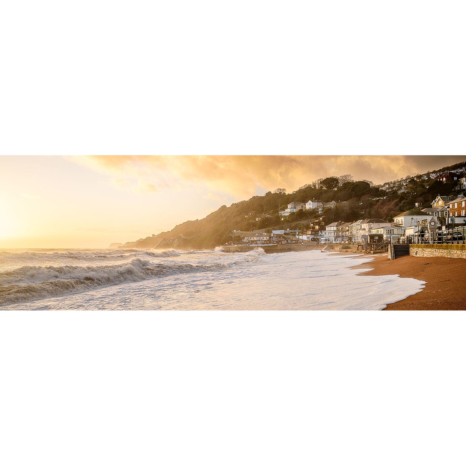Seaside town at sunset with waves rolling onto the beach and the glow of the sun bathing the scene in warm Ventnor light from Available Light Photography.
