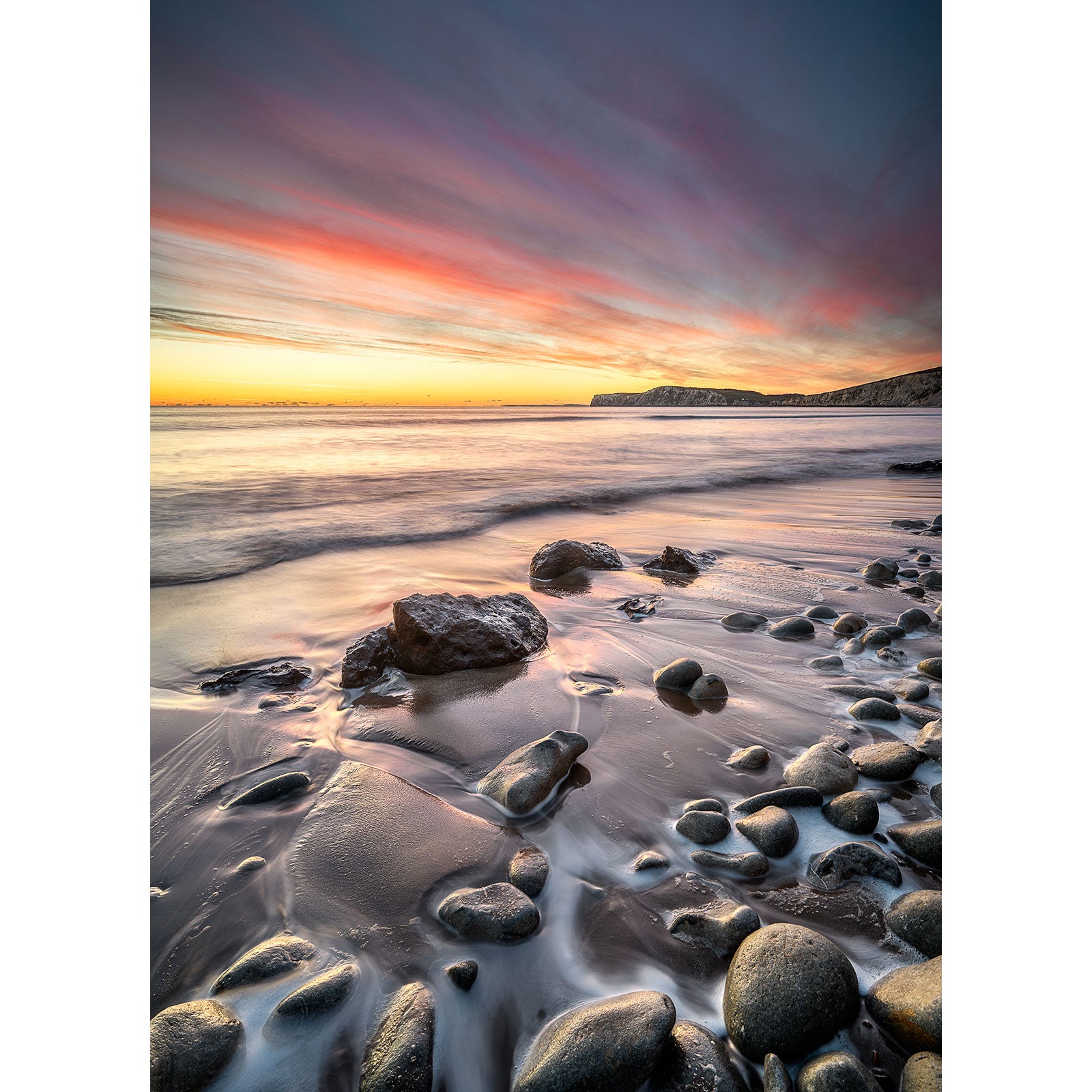 Seaside sunset at Compton Bay on the Isle of Wight with colorful sky and smooth pebbles on wet sand. (Available Light Photography)