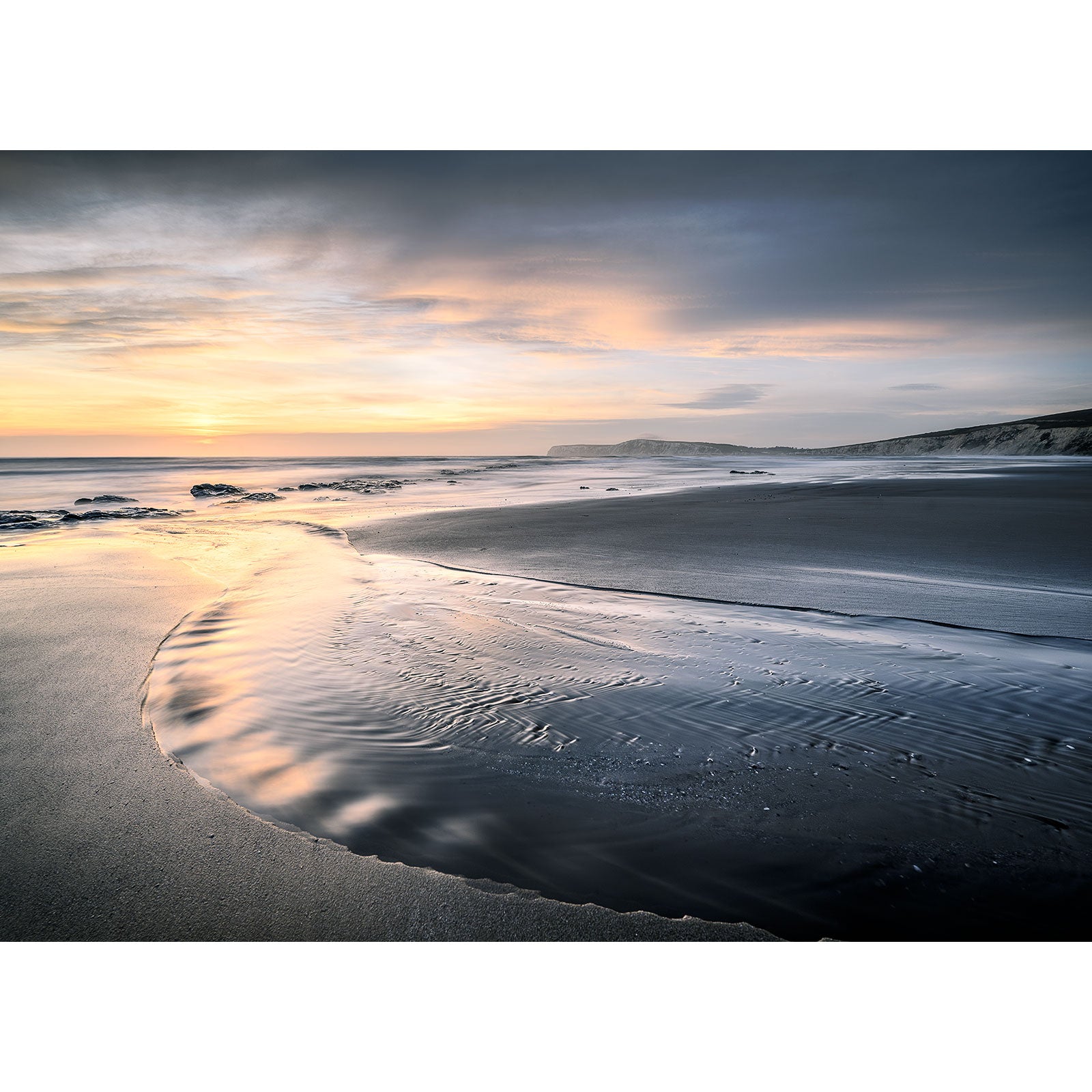 Sunset at Compton Bay, a peaceful beach on the Isle of Wight with gentle waves washing onto the shore and dunes in the background, captured by Available Light Photography.