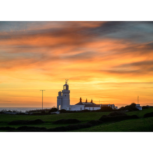 A St. Catherine's Lighthouse and adjacent buildings against a vibrant sunset sky, illuminated by a spectacular afterglow, captured by Available Light Photography.