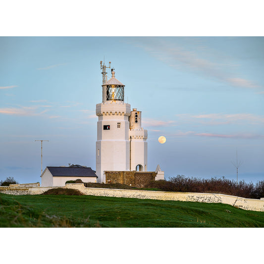 A coastal lighthouse stands prominently, illuminating the surroundings, with Moonrise, St. Catherine's Lighthouse visible in the background at twilight by Available Light Photography.