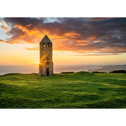 Sunset behind St. Catherine's Oratory, an ancient stone tower on a grassy hill overlooking the ocean, with sun rays piercing through the tower windows captured by Available Light Photography.