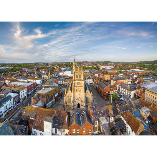 Aerial view of a town center with a prominent church spire, surrounded by clustered buildings and expansive landscapes under a clear sky taken with Newport by Available Light Photography.