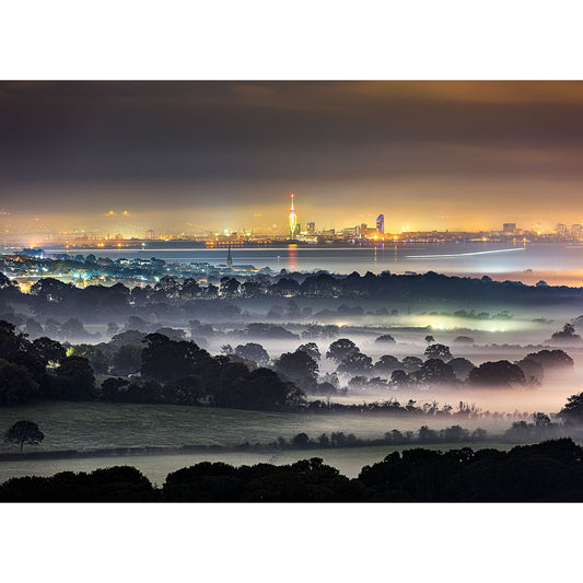 View from Ashey Down by Available Light Photography captures a misty landscape with trees in the foreground and a softly illuminated city skyline glowing at dusk or night.