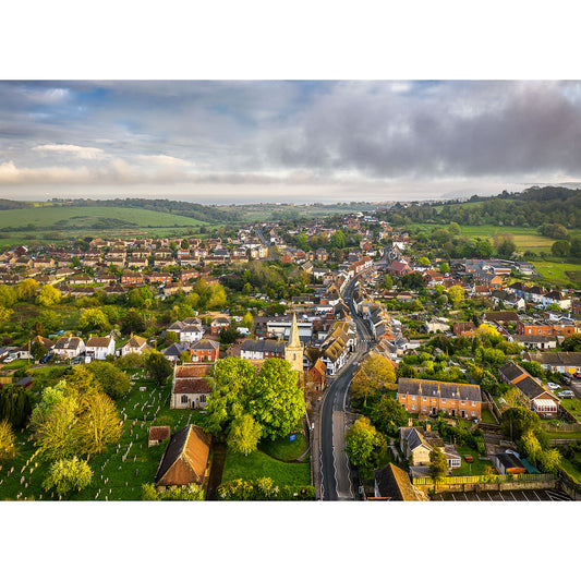 Aerial view of Brading by Available Light Photography captures a peaceful small town with charming houses, a historic church, winding roads, and lush green fields under a partly cloudy sky.