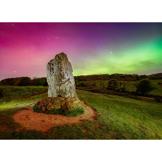 A large standing stone known as the Longstone at Mottistone, set against a vivid night sky lit by the green and pink hues of The Northern Lights, in a lush green field on the Isle of Wight. Captured by Available Light Photography.