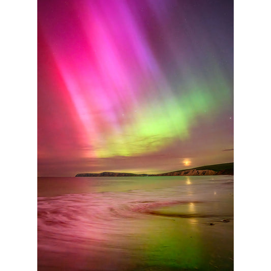 Vivid aurora borealis in purple, pink, and green hues above a moonlit beach with gentle ocean waves and a distant Isle of Wight captured by Available Light Photography's The Northern Lights at Compton Bay.