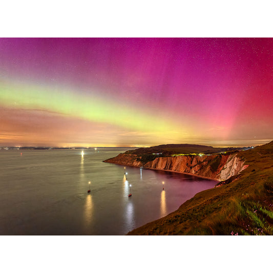 A vibrant aurora borealis over a coastal landscape at night, with cliffs to the right and illuminated boats on the water, creating an unforgettable image number 2858 of The Northern Lights by Alum Bay from Available Light Photography.