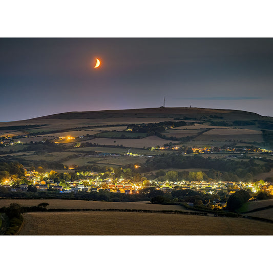Whitwell by Moonlight" by Available Light Photography captures a crescent moon over softly lit houses and fields at dusk, with a distant hill crowned by a tall antenna.