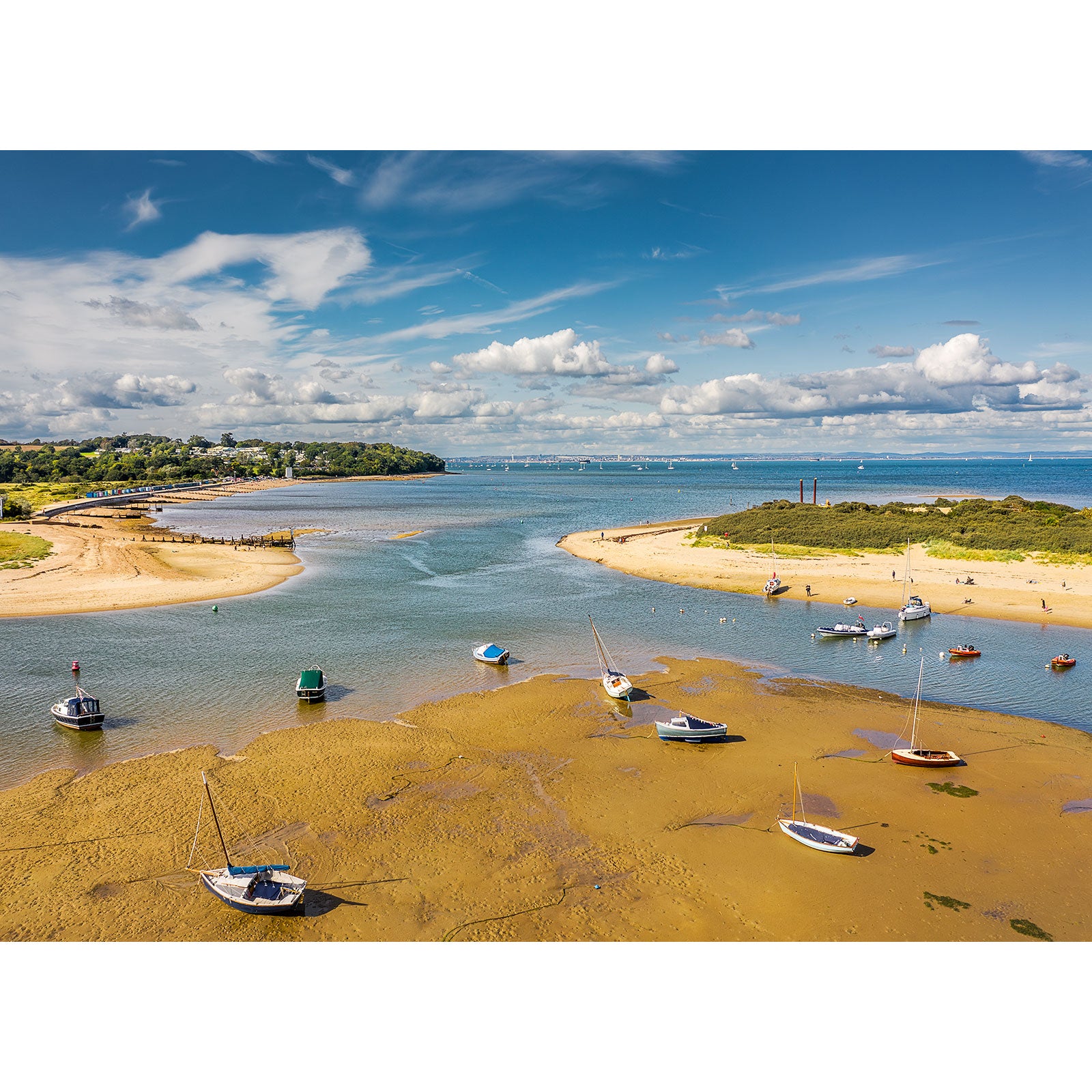 Sailboats rest on sandy banks at low tide in Bembridge Harbour, with distant shores, lush greenery, and scattered clouds, captured by Available Light Photography.