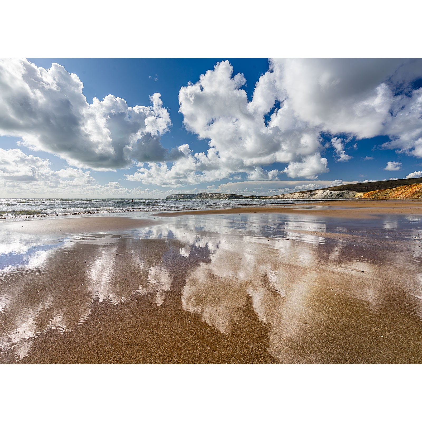 Clouds are reflected in wet sand at Compton Bay, with cliffs in the background beneath a vibrant blue sky. Photo by Available Light Photography.
