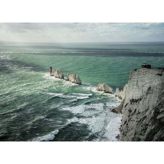 A turquoise sea meets the iconic white chalk cliffs of The Needles, with a red and white lighthouse guiding ships along the dramatic coast. Available Light Photography captures this stunning landscape.