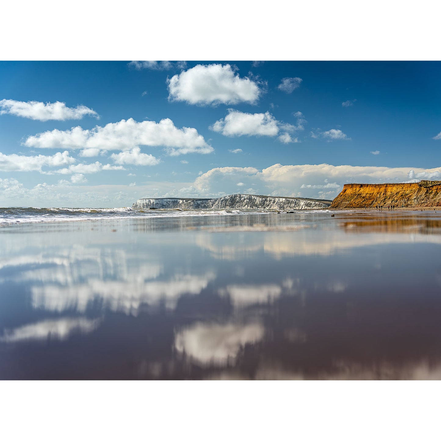 Brook Bay by Available Light Photography captures a sandy beach with gentle waves, distant cliffs, a blue sky with scattered clouds, all reflected on the wet sand.