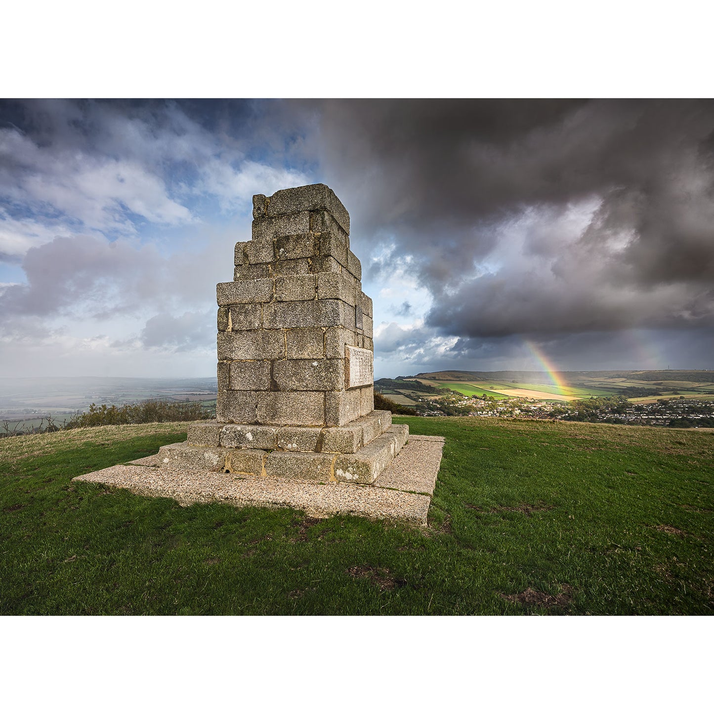 Image number 3081 by Available Light Photography showcases The Worsley Monument atop a grassy hill under cloudy skies, with a distant rainbow spanning the landscape.