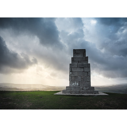 The Worsley Monument by Available Light Photography captures a stone monument atop a grassy hill beneath a cloudy sky, with soft sunlight breaking through in the background, creating a peaceful and timeless atmosphere.