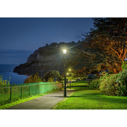 Keats Green, Shanklin by Available Light Photography shows a paved path with street lamps beside lawns and trees, overlooking dramatic cliffs and the calm sea at dusk.