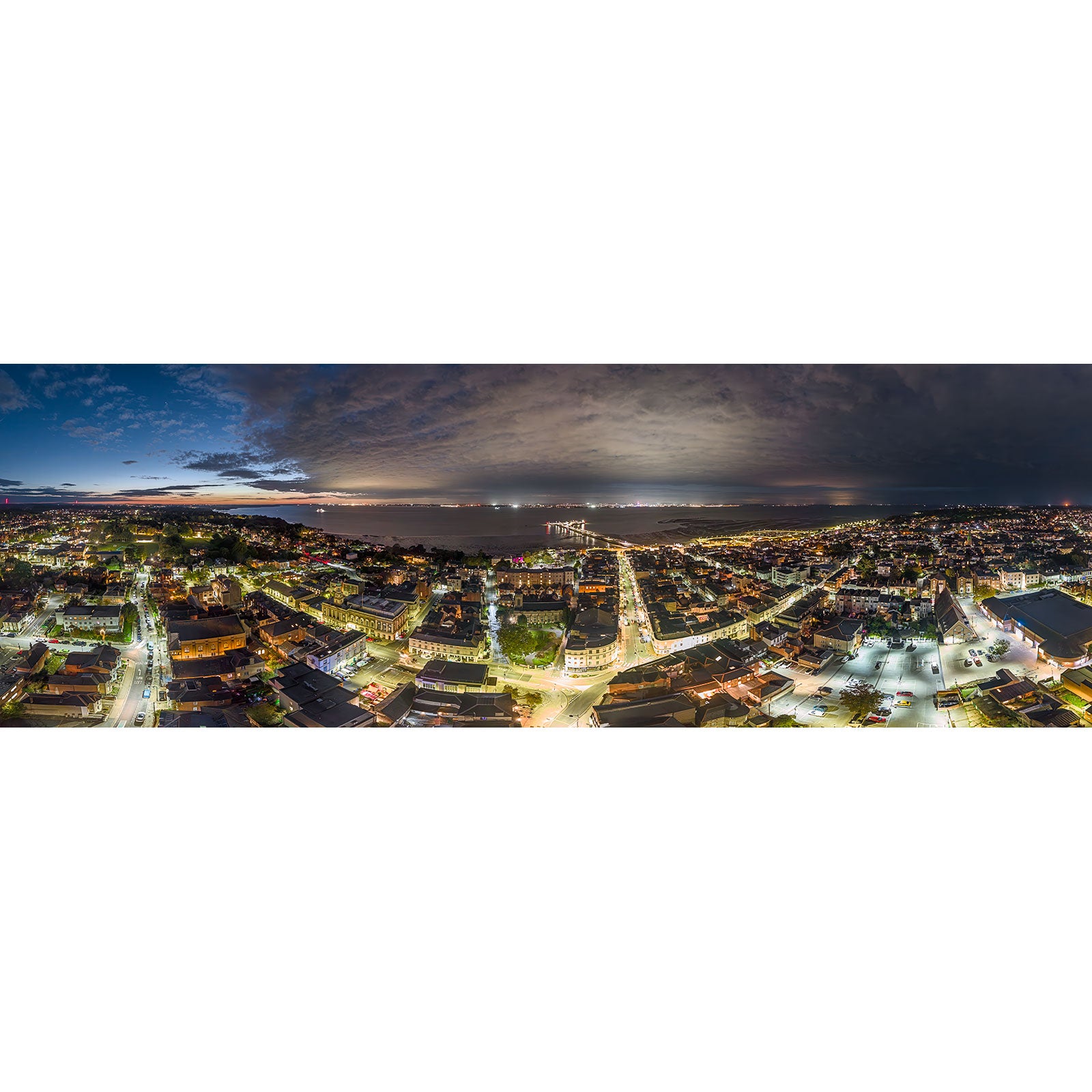 Aerial panoramic view of Ryde at night by Available Light Photography, featuring illuminated streets, buildings, and a dramatic cloudy sky at dusk.