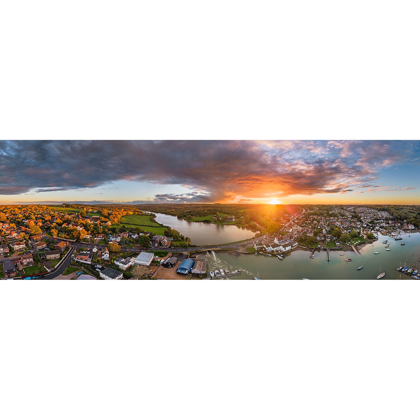 Aerial view of Wootton Bridge at sunset by Available Light Photography, showcasing riverside houses, boats, and a bridge beneath a partly cloudy sky.