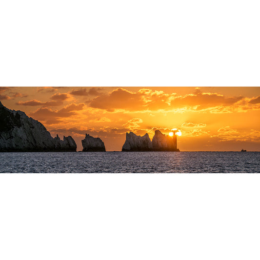 The Needles by Available Light Photography captures rocky sea stacks in silhouette against an orange sunset, with the sun partly visible between formations and tranquil water in the foreground.