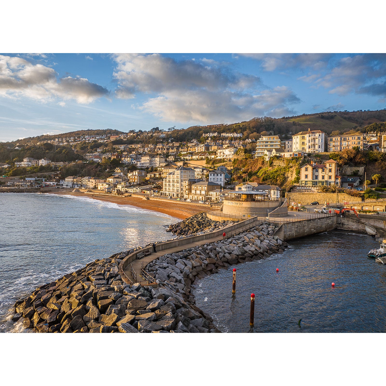 Ventnor seaside town at sunset—houses on a hillside, sandy beach, stone pier, and rocky shoreline—captured by Available Light Photography.
