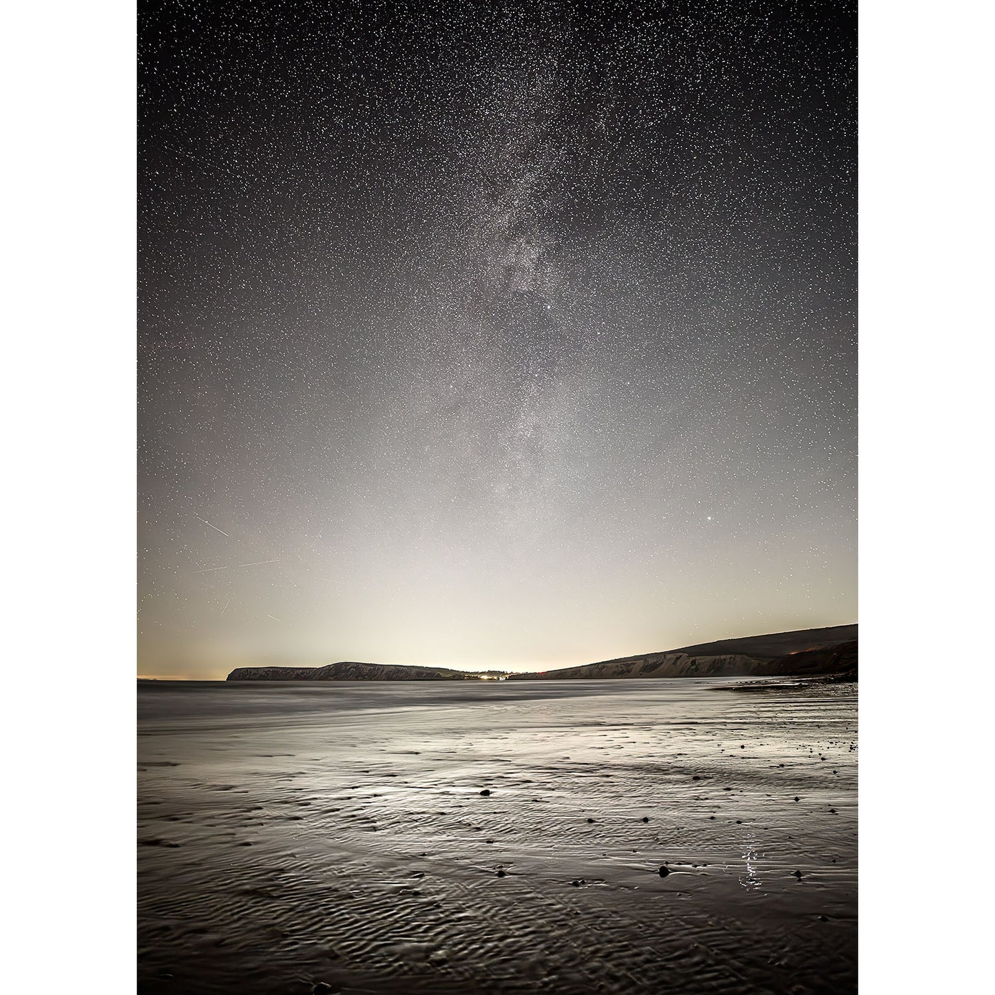 The Milky Way, Compton Bay by Available Light Photography captures a serene night beach scene under a starry sky, with distant cliffs on the horizon and the faint shimmer of the Milky Way above.