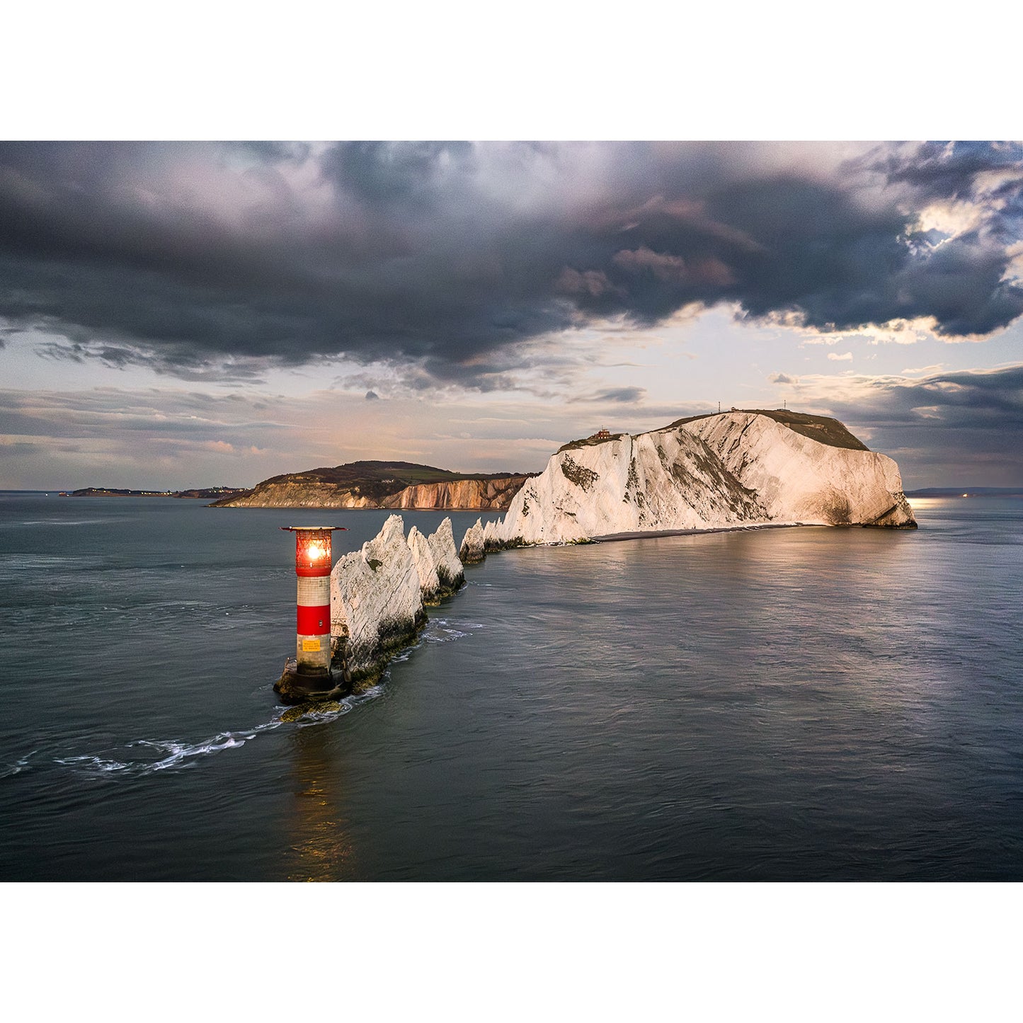 Moonrise over The Needles" by Available Light Photography captures a striking lighthouse with bold red and white stripes beside dramatic chalk rock formations in the sea beneath a cloudy sky.