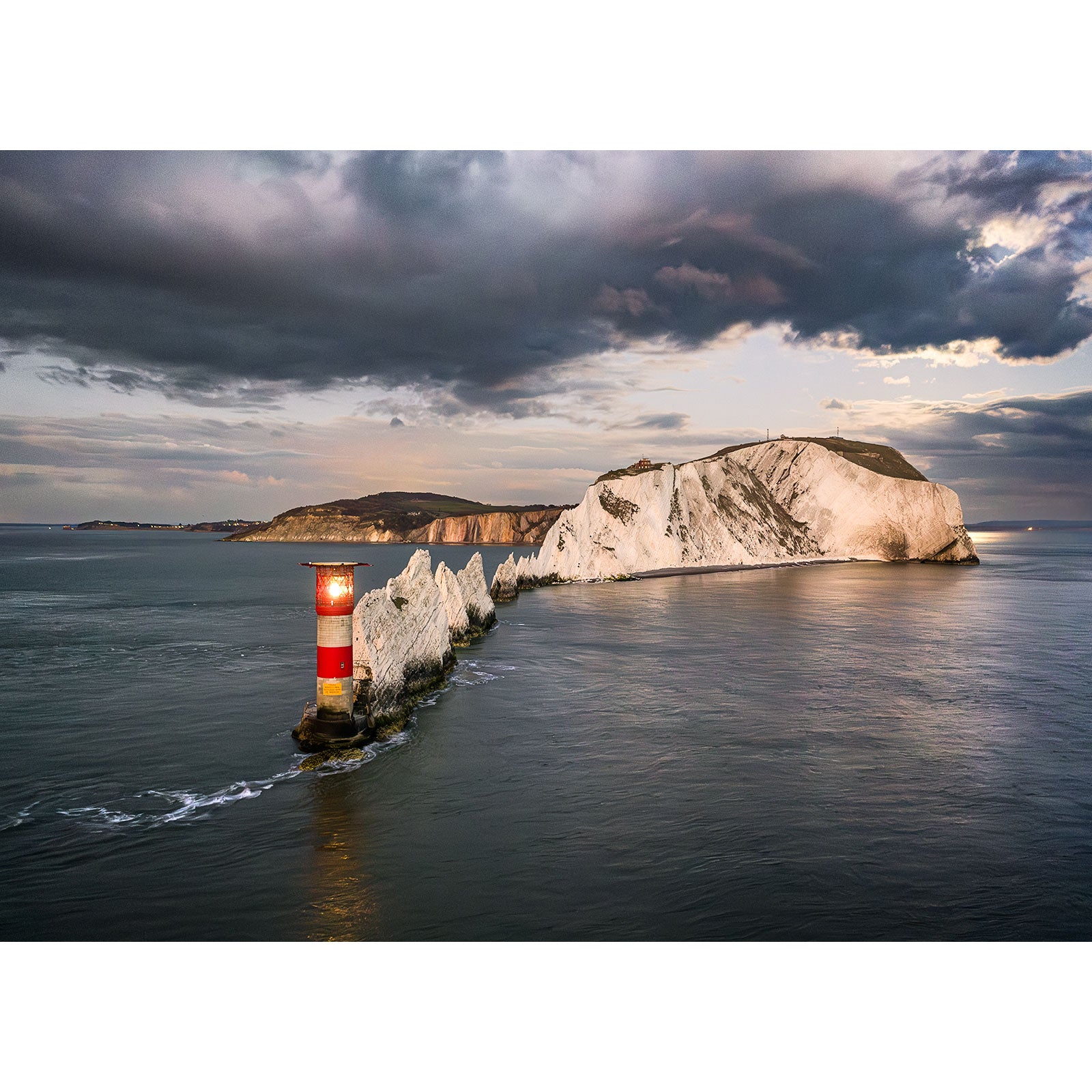 Moonrise over The Needles" by Available Light Photography captures a striking lighthouse with bold red and white stripes beside dramatic chalk rock formations in the sea beneath a cloudy sky.