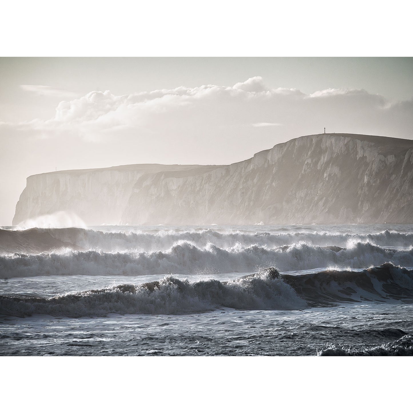 Rough ocean waves crash against the shore at Compton Bay, bordered by steep cliffs and a cloudy sky. Captured by Available Light Photography.