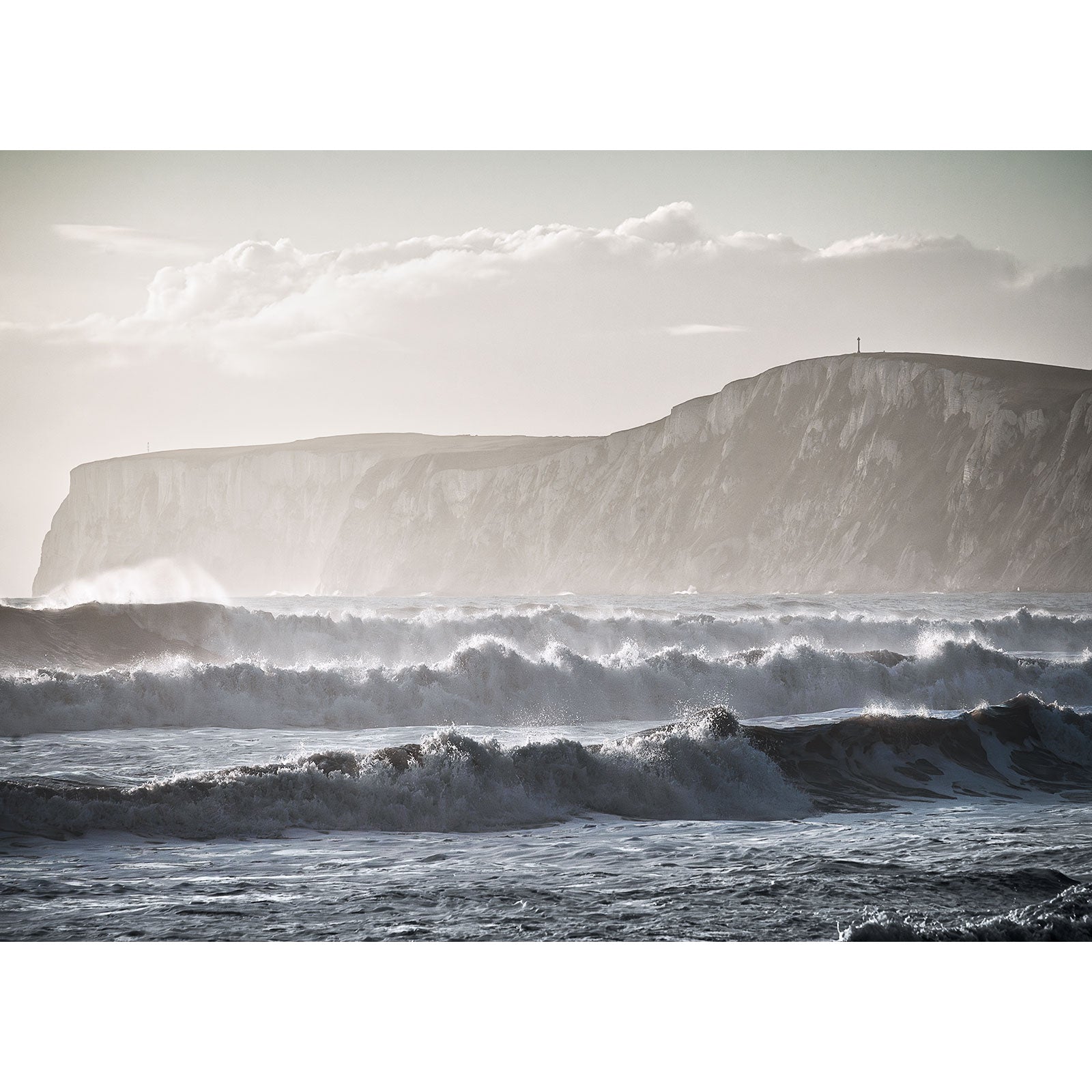 Rough ocean waves crash against the shore at Compton Bay, bordered by steep cliffs and a cloudy sky. Captured by Available Light Photography.