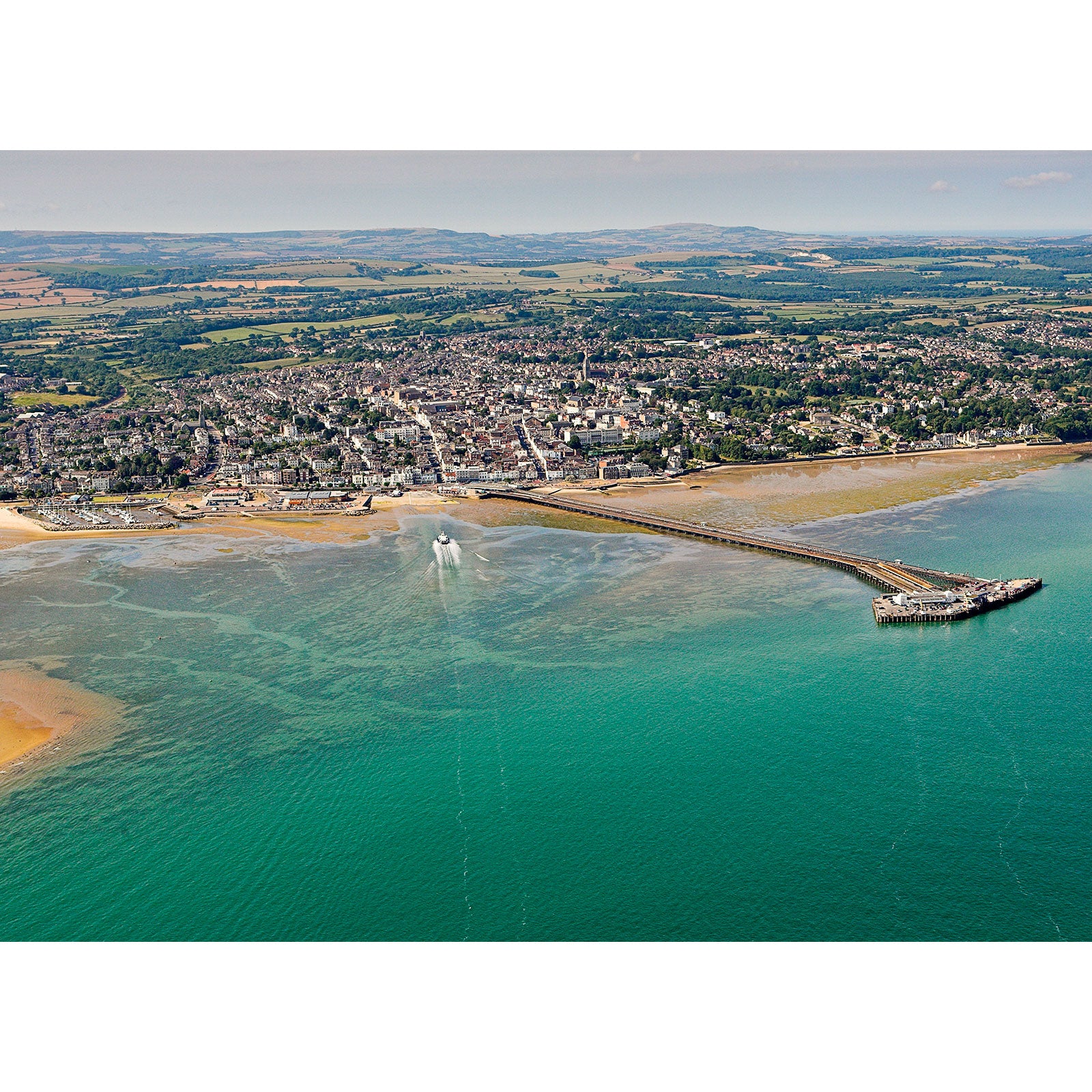 Aerial view of Ryde, a coastal town on the Isle with a pier, clear shallow waters, and surrounding greenery captured by Available Light Photography.