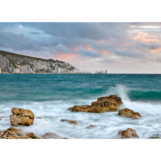 A coastal landscape at dusk with choppy seas, rocky foreground, and The Needles cliffs in the background under a cloudy sky by Available Light Photography.