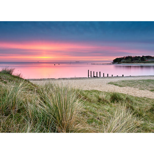 Sunset over a calm sea viewed from a grassy shoreline on The Duver, St. Helens by Available Light Photography.