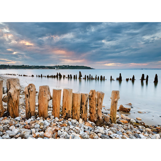Bembridge Beach wooden posts on a pebble beach at twilight with calm water and cloudy skies in the background on the Isle of Wight by Available Light Photography.
