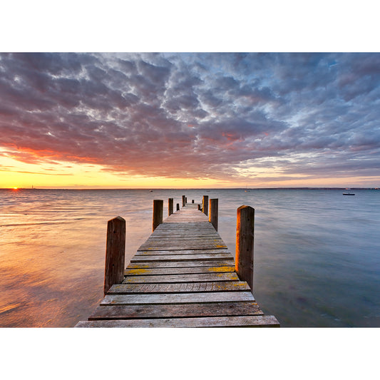 A wooden pier extending into calm waters under a dramatic sunset sky on The Solent by Available Light Photography.