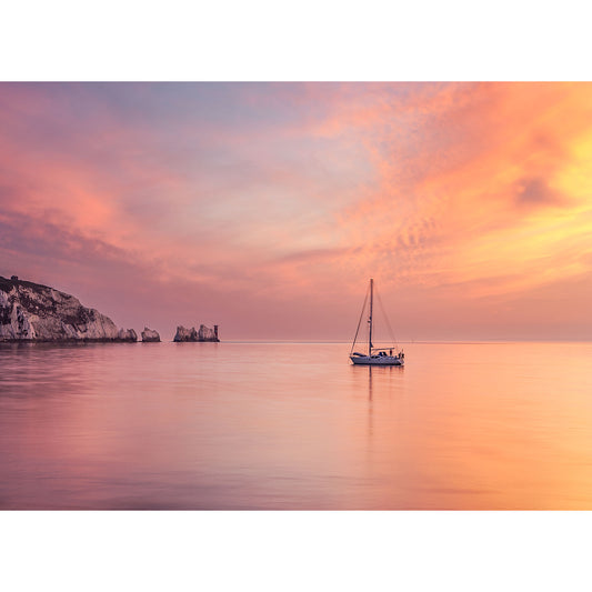 A sailboat drifting on calm waters during a serene sunset with cliffs in the distance on the Isle of Wight captured by Available Light Photography's The Needles print.