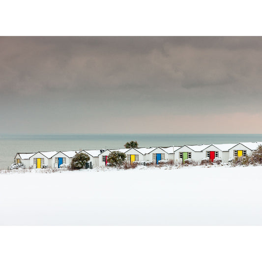 Row of colorful beach huts against a Winter, Brighstone foreground on the Isle of Gascoigne with a dark stormy sky overhead, captured by Available Light Photography.