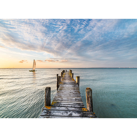 A tranquil scene showing an aged wooden pier extending into the sea near the Isle of Wight, with a sailboat in the distance under a wide sky with scattered clouds captured by The Solent from Available Light Photography.