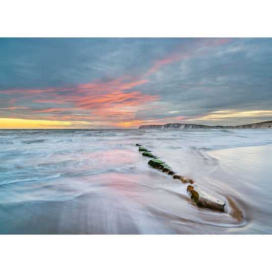 Sunset over Compton Bay on the Isle of Wight with waves flowing around a wooden breakwater by Available Light Photography.