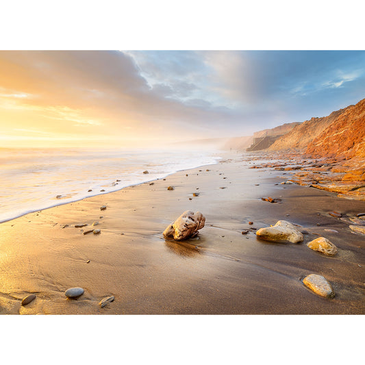 Sunset illuminates a tranquil Compton Bay beach on the Isle with scattered rocks and cliffs in the distance by Available Light Photography.