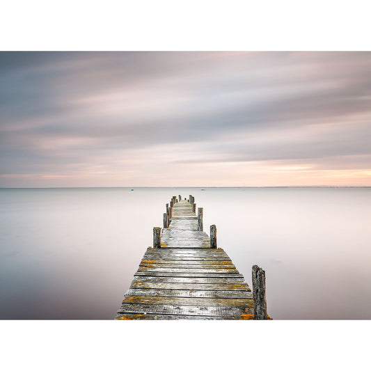 A serene long exposure photograph of The Solent, an old wooden pier extending into a calm sea under a softly colored sky on the Isle of Wight by Available Light Photography.